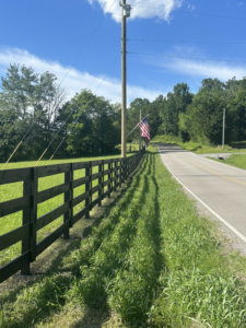 A black wooden fence running alongside a road with an American flag, a project by Pileggi Fence Painting in Franklin, TN