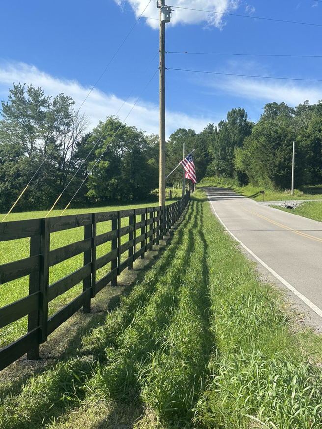 A black wooden fence running alongside a road with an American flag, a project by Pileggi Fence Painting in Franklin, TN
