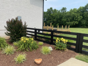 A black wooden fence bordering a landscaped area next to a house, a project by Pileggi Fence Painting in Franklin, TN