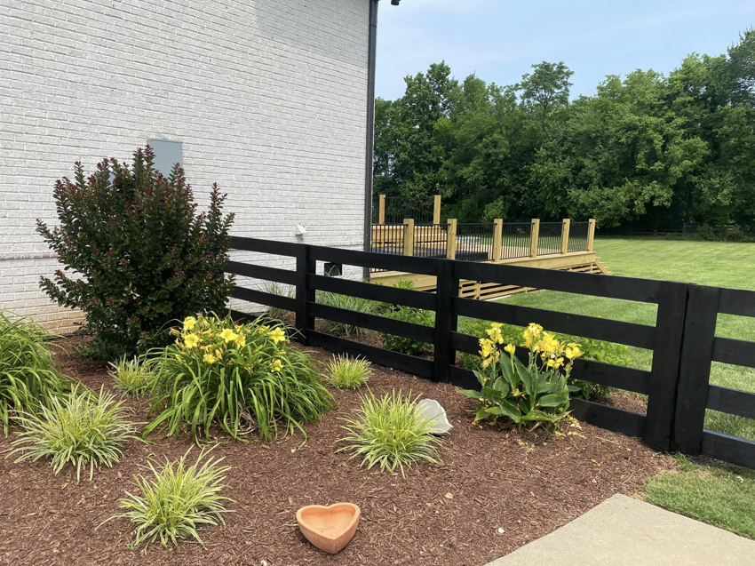 A black wooden fence bordering a landscaped area next to a house, a project by Pileggi Fence Painting in Franklin, TN