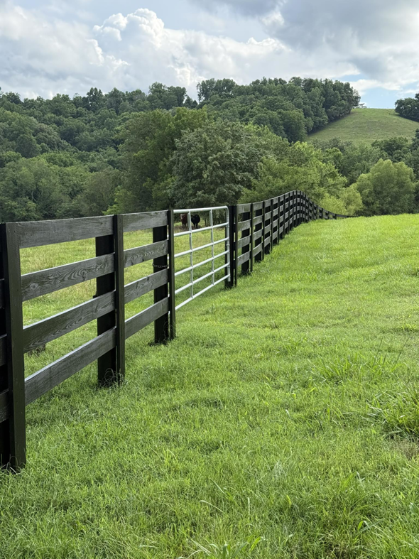 A long black wooden fence with a metal gate installed in a grassy field by The Fence Painter in Lynnville, TN.