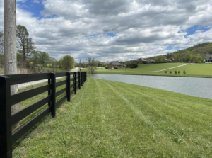 A black wooden fence installed next to a scenic pond, showcasing work by Pileggi Fence Painting in Franklin, TN