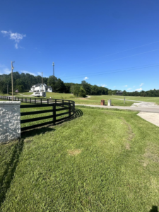 A black wooden fence with a stone pillar entrance leading to a property, installed by Pileggi Fence Painting in Franklin, TN