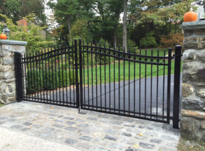 A black wrought iron style driveway gate with stone pillars, installed by Ozark Fence in Lakewood, CO.