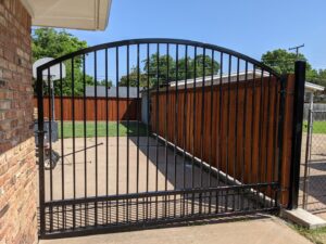 A custom black wrought iron gate with an arched top and wood fence installed by Pro Insulation and Fence in Wichita Falls, TX.