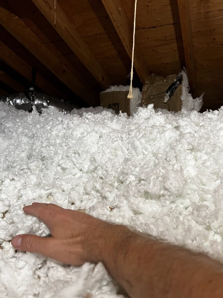 A hand demonstrating the depth of blown-in attic insulation installed by EZ Comfort Air Conditioning & Heating LLC in Humble, TX.