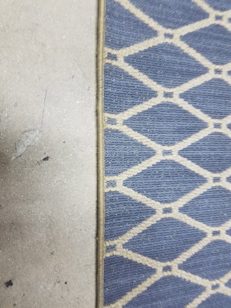 Close-up of a blue patterned rug edge on a concrete floor from Palmetto Carpet Company in Miami, FL.