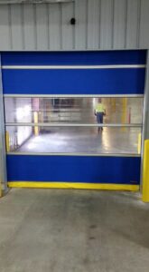 A blue and yellow high-speed commercial roll-up door with clear panels, installed by Tri County Overhead Door Service Inc in New London, WI