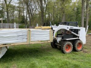 A Bobcat skid-steer loader moving a crate of fencing materials for Texeira Fencing & Concrete in Springfield, MA.