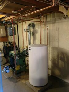 A green boiler/furnace unit with an expansion tank and a white hot water heater installed by Nate's Oil Burner Service in New Bedford, MA
