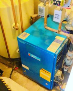 A blue boiler unit with copper piping and a water heater tank installed by Deboque Duct Design Corp. in Staten Island, NY