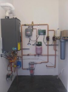 A complex heating system with a wall-mounted boiler and extensive copper piping by Boiler Man Plumbing & Heating in Palmer, AK