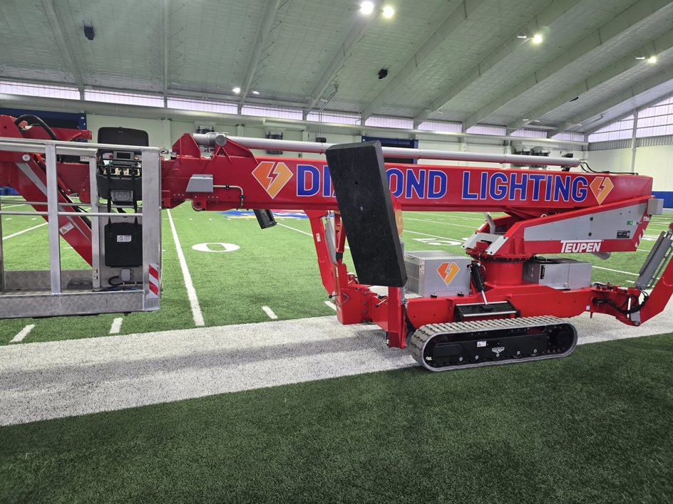 A red boom lift from Diamond Lighting & Maintenance positioned for indoor lighting maintenance at a sports facility in Sheridan, IL.