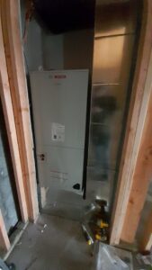 A Bosch air handler unit being installed within a framed wall cavity, showing ductwork, by PNW Spokane Heating and Air in Spokane, WA.
