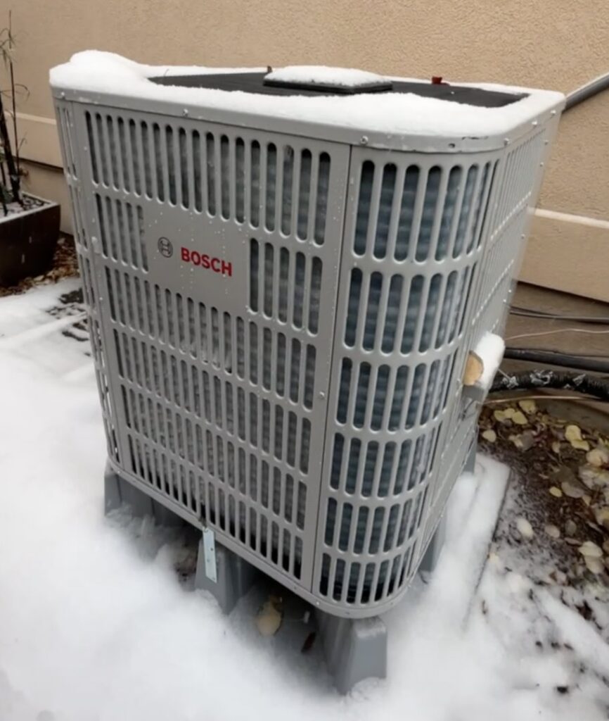 A Bosch heat pump outdoor unit operating efficiently in snowy conditions, installed by Just Heat Pumps in Denver, CO.