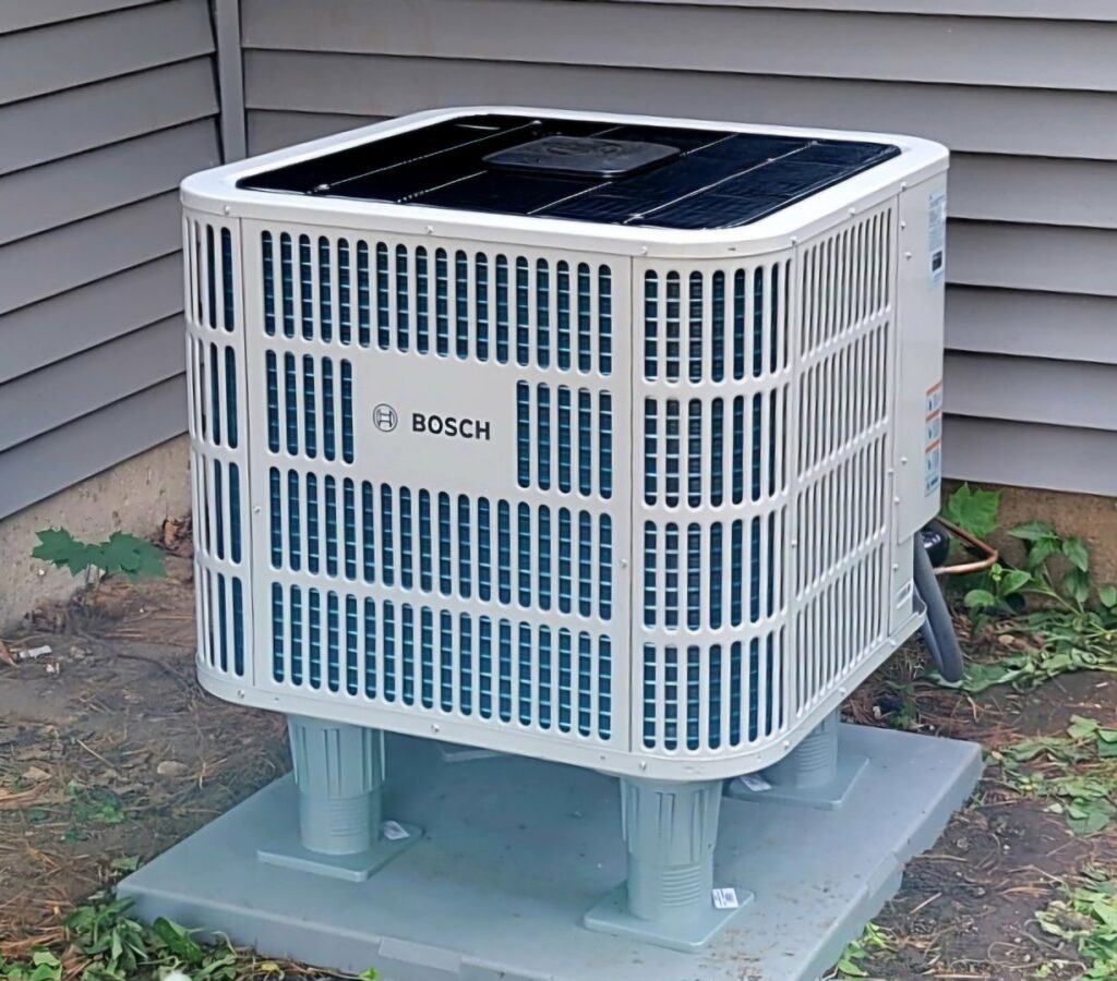 A Bosch outdoor air conditioning unit installed on risers next to a residential building by Kerley Heating & Cooling in Rock City, IL