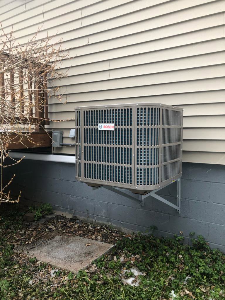 A Bosch outdoor air conditioning unit wall-mounted on a residential building by Simply Installs Heating & Air Conditioning in Shortsville, NY.