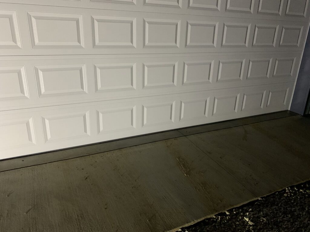 A close-up of the bottom panel and weather seal of a white garage door, installed or repaired by Affordable Overhead Garage Door in Modesto, CA