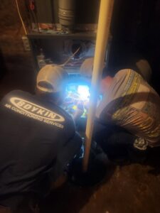Two Boykin Air Conditioning Services technicians servicing an indoor furnace or air handler in Sumter, SC.