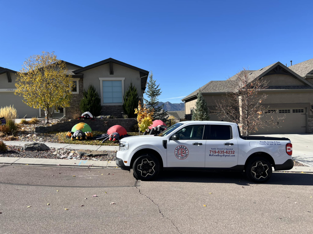 A white Academy Pest Control branded truck parked in front of a residential home in Colorado Springs, CO.