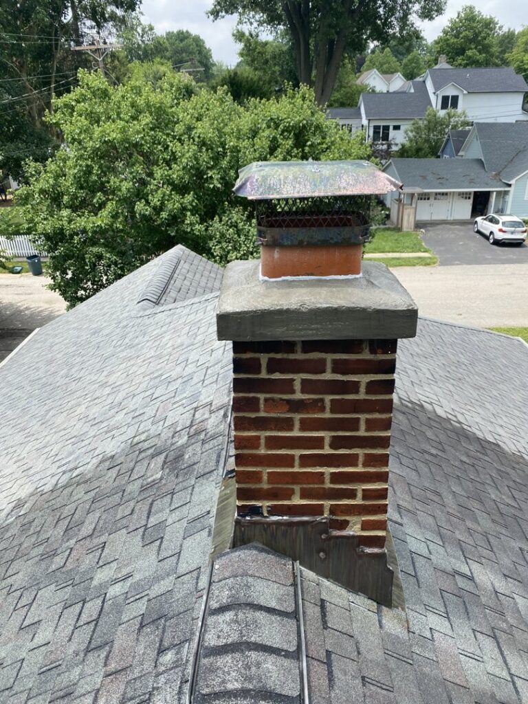 A brick chimney with a metal cap on a residential roof, indicating a chimney inspection or repair by Indy Ignited in Indianapolis, IN.