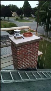 A brick chimney on a rooftop with scaffolding and a ladder, indicating chimney sweep or repair work by Buffalo Chimney Sweep in Buffalo, NY.