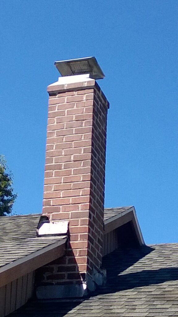 A sturdy brick chimney with a protective cap on a residential roof by Burning Bush Chimney Service in Wood Village, OR.