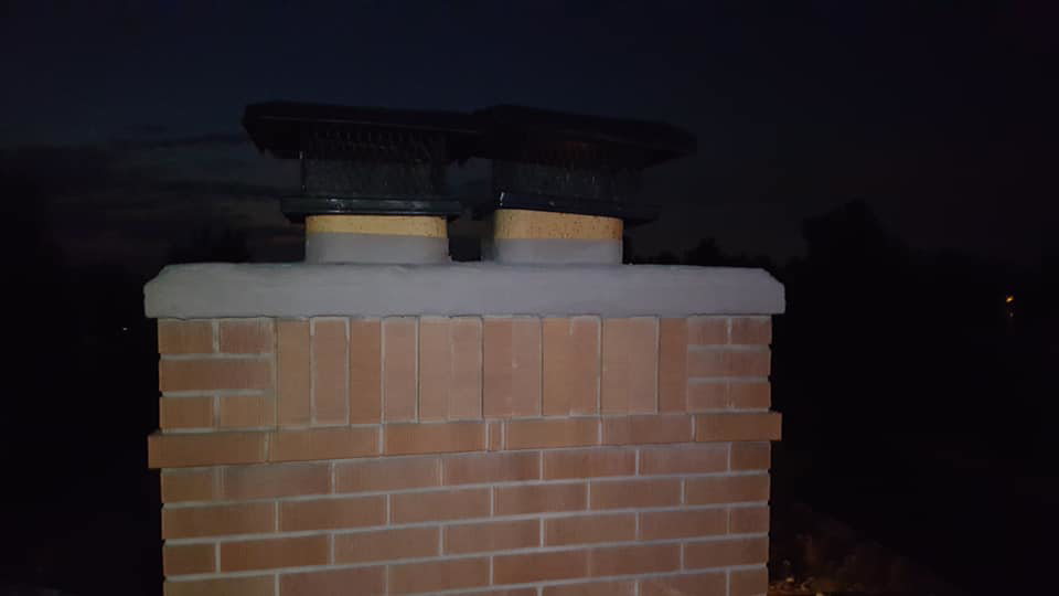 A brick chimney with two new chimney caps installed at night by Chimney Karma in Fort Collins, CO.