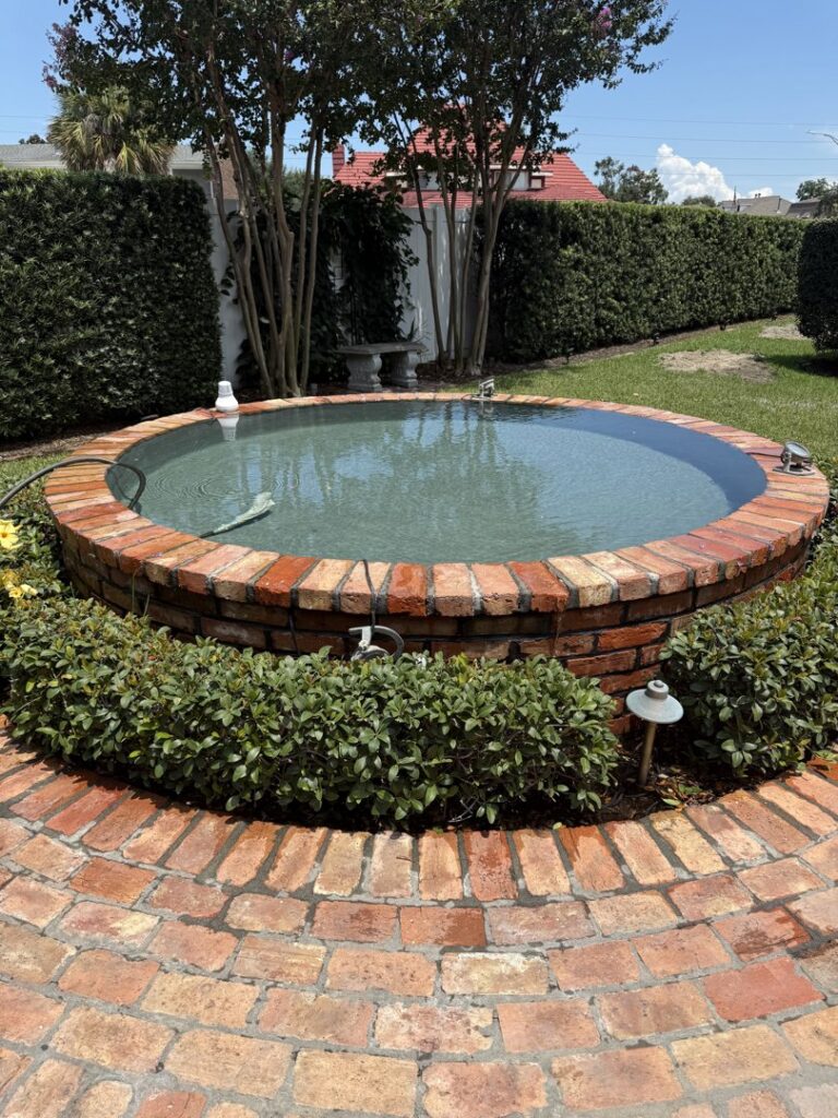 A circular brick water feature or small pool with clear water, completed by I10 Pool Plastering LLC in Kenner, LA.