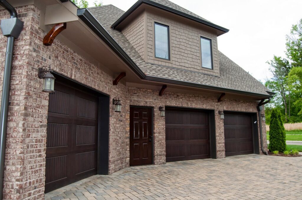 A traditional brick home showcasing three dark brown garage doors installed by Magic City Door Huntsville in Birmingham, AL.