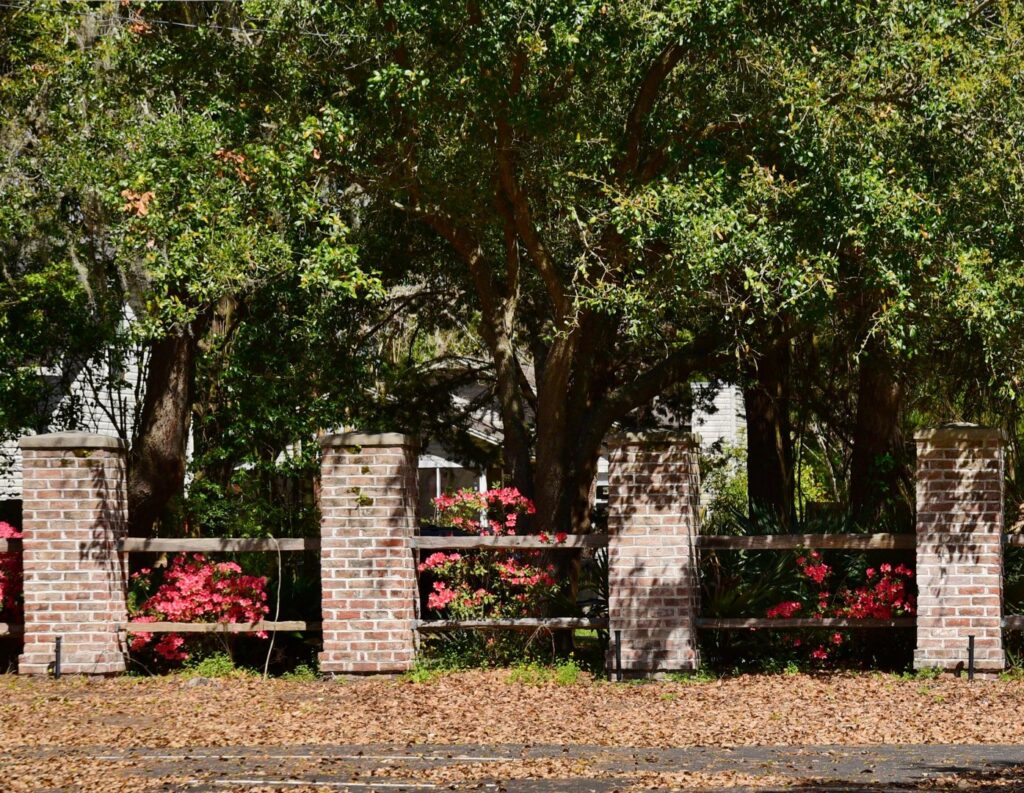 A decorative fence featuring brick pillars and wooden rails with flowering bushes, installed by Five Star Fence in Charleston, SC.