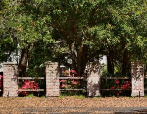 A decorative fence featuring brick pillars and wooden rails with flowering bushes, installed by Five Star Fence in Charleston, SC.