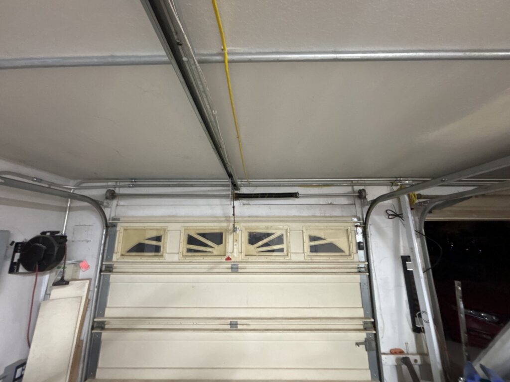 An old garage door with a clearly broken spring, indicating a repair job for Olympus Garage Door Repair in Tempe, AZ.