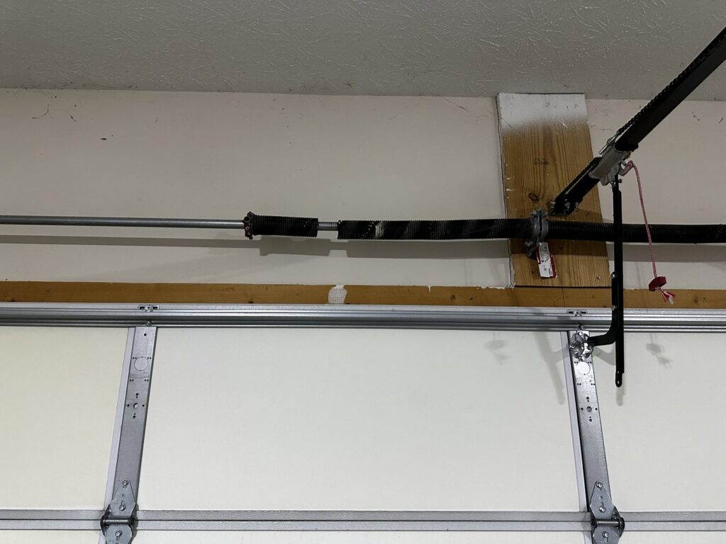 A close-up view of a broken garage door torsion spring, indicating a repair job by Steve's Overhead Door Company in Lafayette, IN.