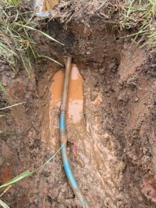 A broken water pipe in a muddy trench requiring repair by Komfort Air Service Experts in Charlotte, NC.
