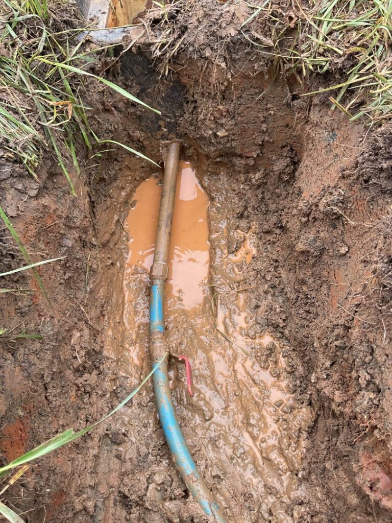 A broken water pipe in a muddy trench requiring repair by Komfort Air Service Experts in Charlotte, NC.