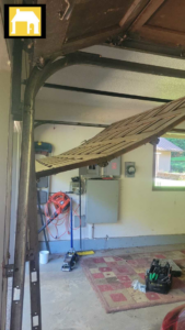 Broken wooden garage door hanging from tracks inside a garage, repaired by TH Locksmith And Garage Door Repair, Vancouver, WA.
