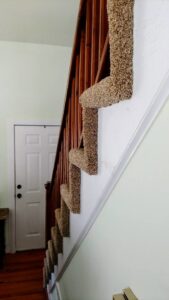 A professionally installed brown carpet stair runner, wrapped around balusters, by Prestige Flooring in Auburn, AL.