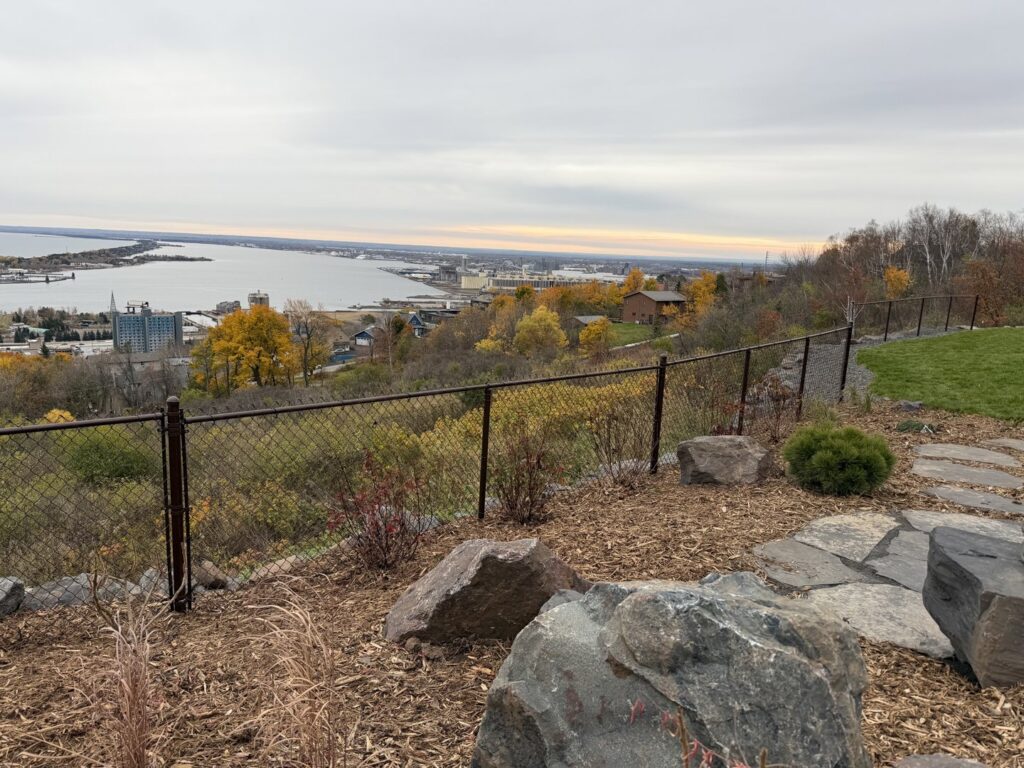 A brown chain-link fence installed on a hillside overlooking a city by North Shore Fence Company in Centereach, NY.