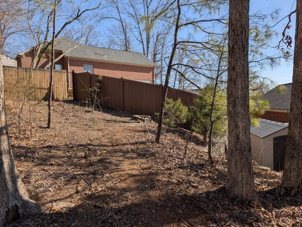 A brown composite fence installed on sloped terrain in a residential area by Alabama's Fencing in Huntsville, AL.