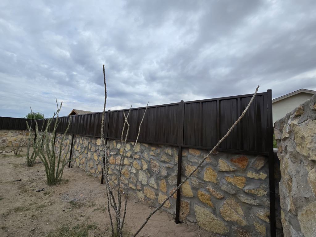 A brown corrugated metal privacy fence with a stone base by Iron Man Exteriors in Las Cruces, NM.