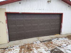 A newly installed brown garage door on a white-sided house, showcasing work by Max Garage Door in Minneapolis, MN.