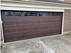 A newly installed brown garage door with windows on a brick home by Overhead Door Company of Evansville in Evansville, IN.