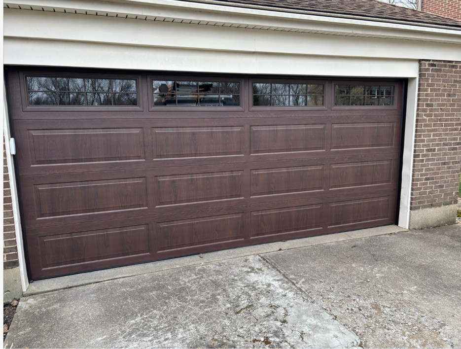 A newly installed brown garage door with windows on a brick home by Overhead Door Company of Evansville in Evansville, IN.