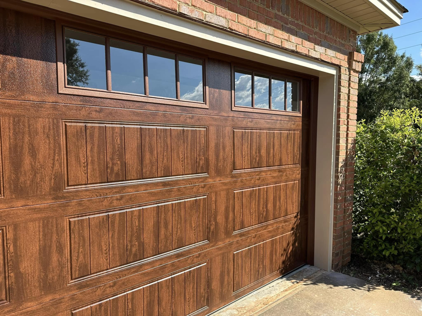 A brown garage door with windows on a brick house, installed by Mike's Garage Door Repair in Wetumpka, AL.