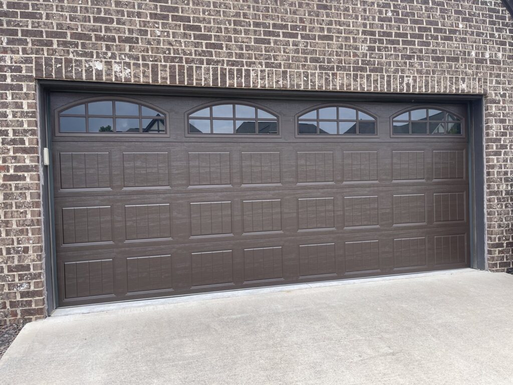 A newly installed brown garage door with arched windows on a brick home by Foothills Garage Door Service LLC in Louisville, TN.