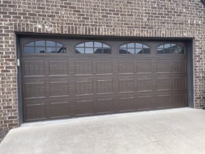 A newly installed brown garage door with arched windows on a brick home by Foothills Garage Door Service LLC in Louisville, TN.