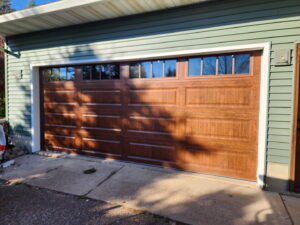 A brown garage door with windows installed on a house with light green siding by LabraDoor Overhead Services in Eau Claire, WI.