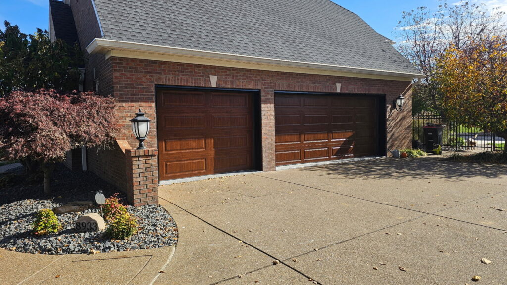 Two brown garage doors on a brick house with landscaping, installed by A+ Garage Door Repair in Evansville, IN.