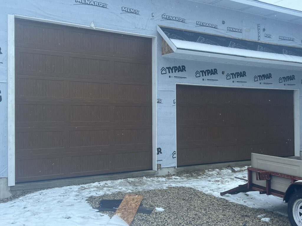 Two brown garage doors installed on a house under construction, showcasing work by McDonald Overhead Door Inc. in Kenosha, WI.